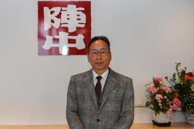 社章の前に立つ社長